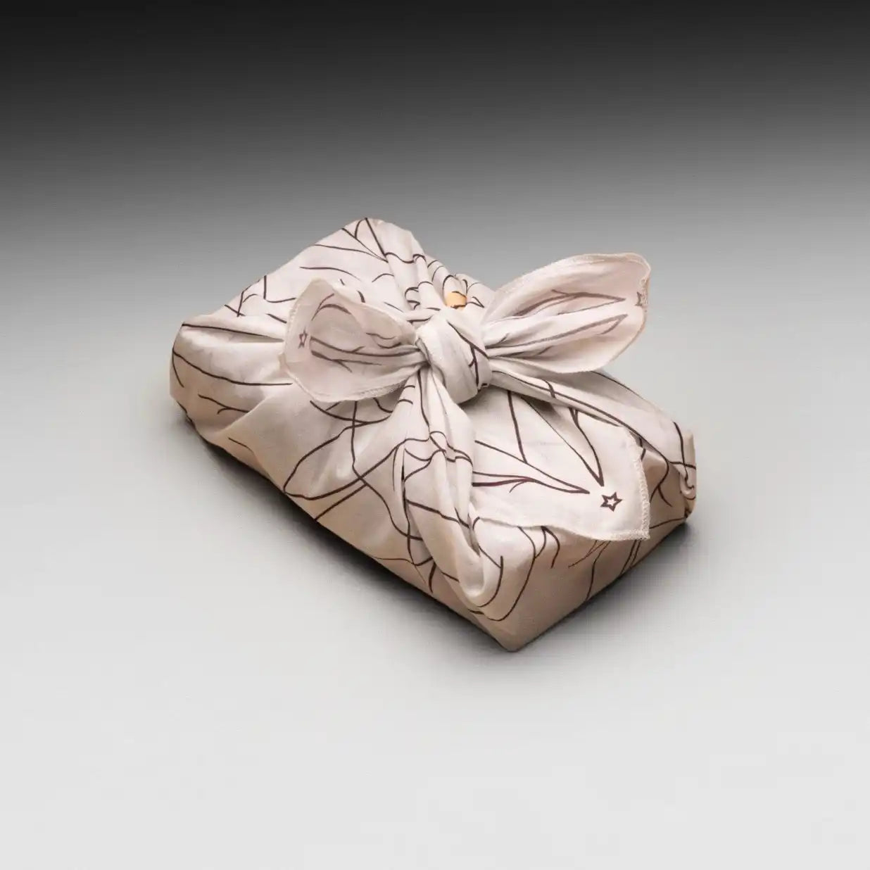 A light-colored fabric gift wrap with a black line-drawn floral pattern, tied with a bow.