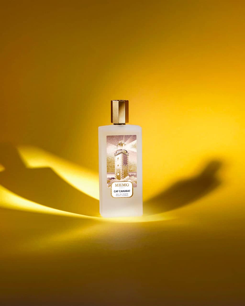 A frosted glass perfume bottle with a gold cap and label featuring a lighthouse illustration, branded as ’memo cap cana’ by memo.