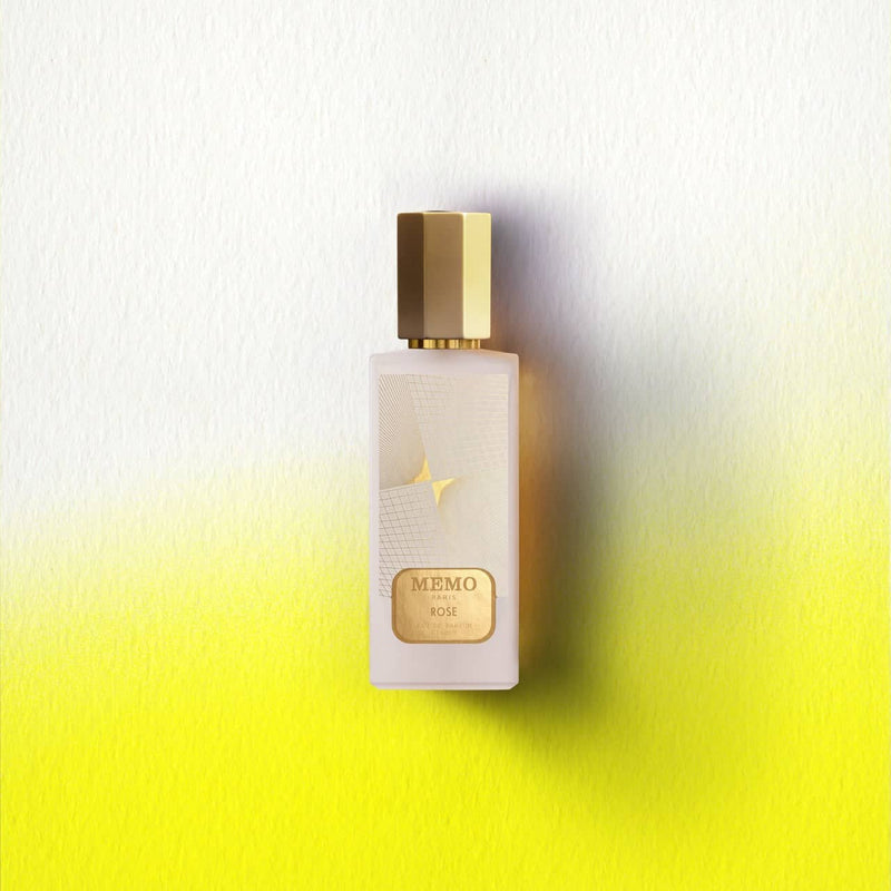 A sleek, frosted glass perfume bottle with a gold hexagonal cap and label, featuring the ’memo paris rose’ branding.