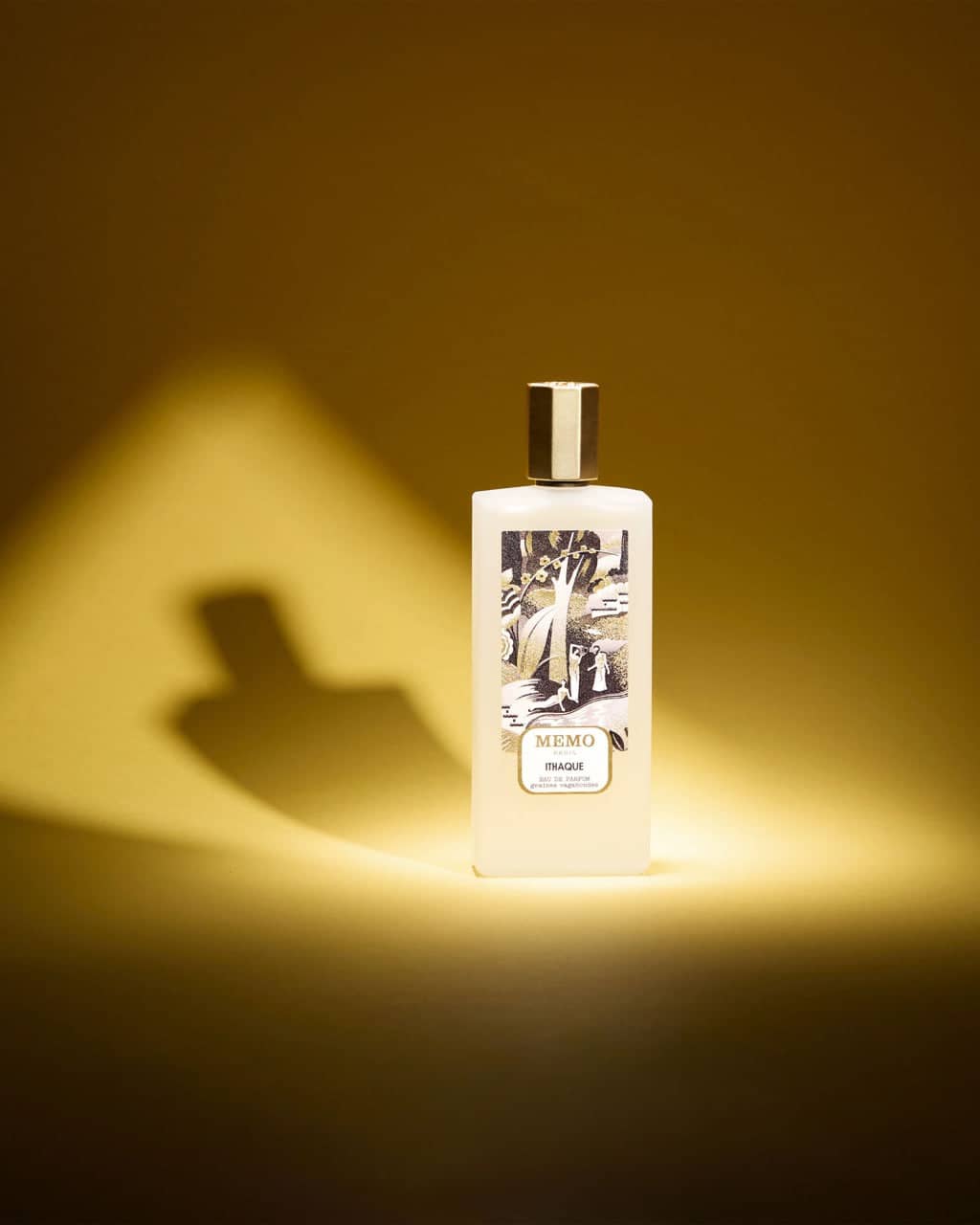 A white rectangular bottle of memo fragrance with a gold cap and an illustrated label depicting figures in a landscape.